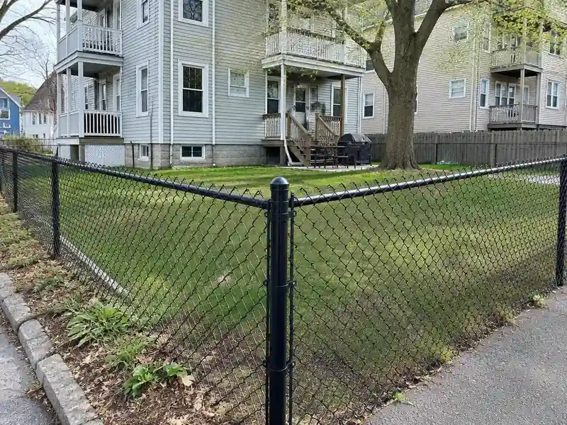 Black vinyl-coated chain link fence around a triple-decker yard in Massachusetts