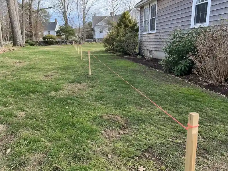 Fence line marked with stakes and string along a suburban lot in Greater Boston
